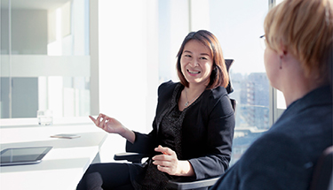 Two professional women congenially have a discussion in boardroom.