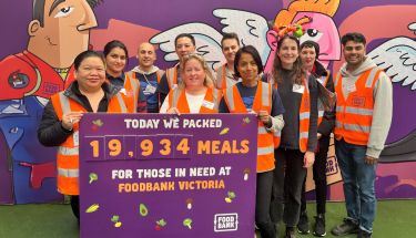 Feeding our community: A group of volunteers in orange vests holding a sign saying how many meals they packed at foodbank Victoria for the day