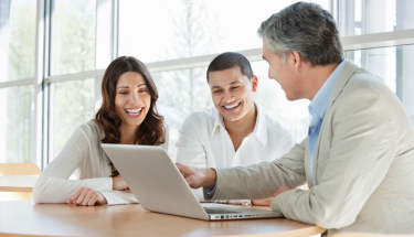 Financial consultant advising a happy young couple while using a laptop