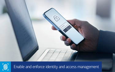 “Enable and enforce identity and access management” A man’s hand holding a cell phone in front of a laptop computer.