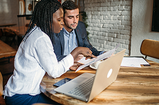 A man and woman reviewing documents in front of a laptop computer.