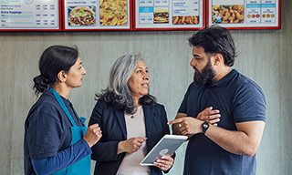 Three fast food restaurant employees talking beneath menus.