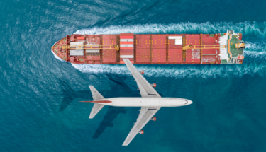 Passenger plane flying over the sea with cargo ship sailing on the sea