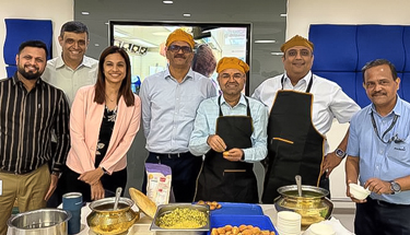 A group of employees standing at the back of a table full of food.