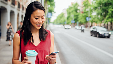 Young girl outside looking at her phone in one hand and holding coffee cup in other