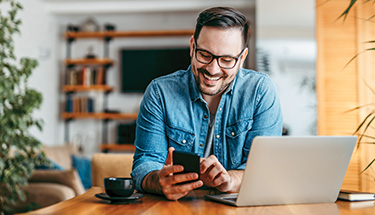Man sitting at desk smiling and looking at something on his phone 