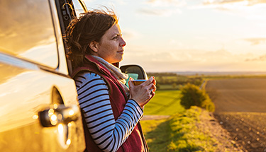 Woman standing against her vehicle at dawn holding her coffee and enjoying the scenery