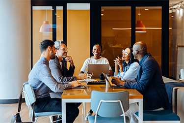 Three men and two women smiling and laughing in a meeting in a work conference room.