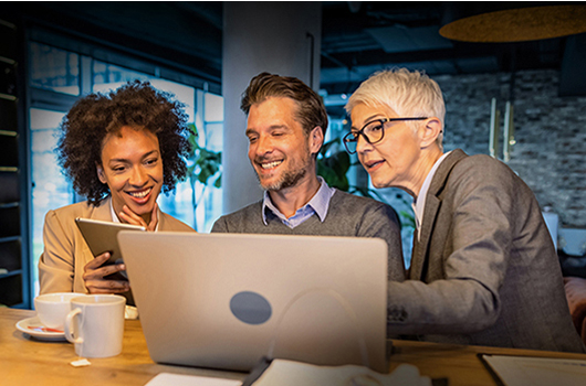3 people sitting together looking at a laptop